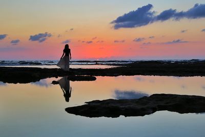 Woman standing at beach against sky during sunset