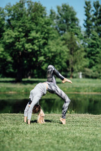 Full length of young woman exercising by pond on field