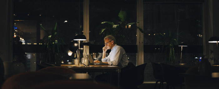 Side view of senior male entrepreneur working late in dark coworking space