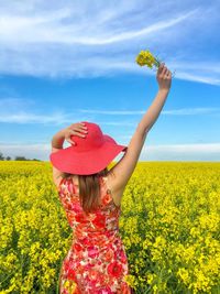 Rear view of woman standing on oilseed rape field against sky