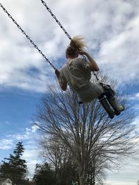 Low angle view of girl enjoying on swing against cloudy sky