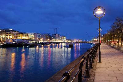 Illuminated street lights by river against sky at night