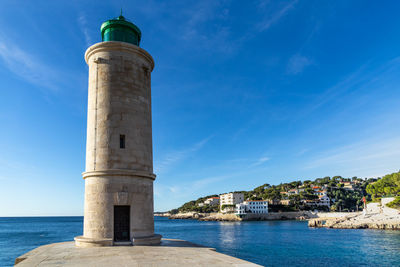 Lighthouse by sea against blue sky