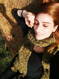 Portrait of smiling young woman against tree trunk / woman smiling / happy woman