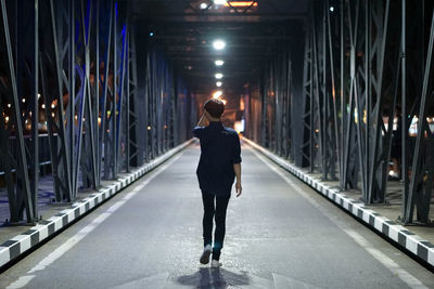 Rear view of man walking on illuminated footpath at night