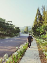 Rear view of man walking on road against clear sky