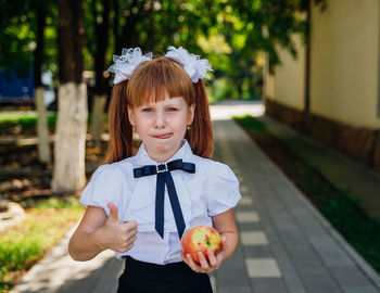 Back to school. a little schoolgirl stands in the school yard and holds an apple in her hands.
