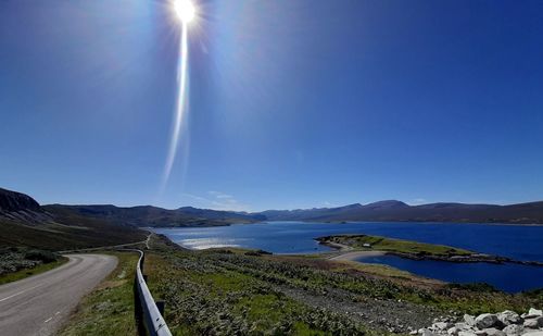 Panoramic view of road by sea against blue sky