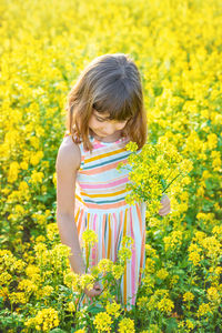 Side view of woman standing amidst yellow flowering plants on field