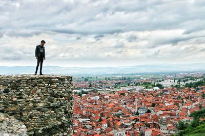 Man standing on wall over townscape against sky