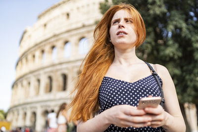 Young female traveler using smartphone and looking away