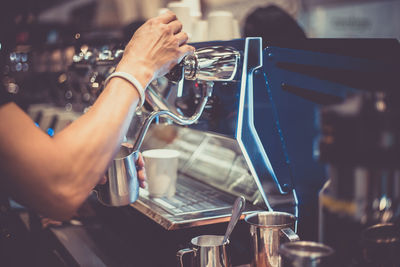 Cropped hand filling jug with drink in cafe