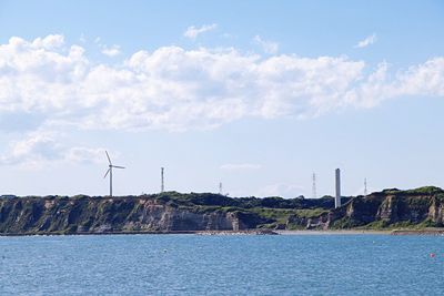 Traditional windmill by sea against sky