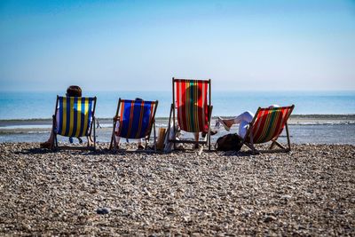 Rear view of people sitting on deck chairs at beach