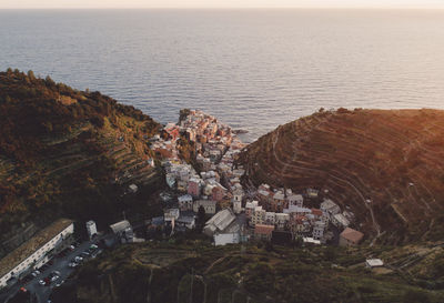 Aerial view of cityscape amidst mountains against sea during sunset