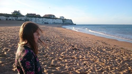 Thoughtful woman standing at beach against sky