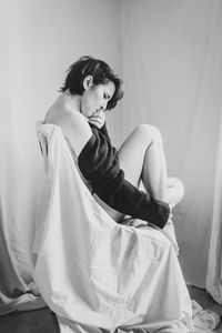 Side view of woman sitting on bed at home