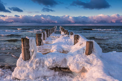 Frozen wooden posts in sea against sky