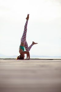 Full length of mid adult woman doing headstand against clear sky