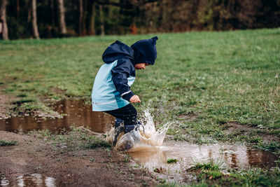 Full length of boy with umbrella in puddle