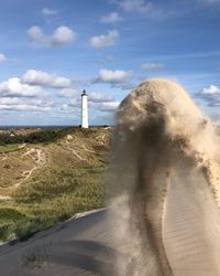 Lighthouse amidst sea and buildings against sky