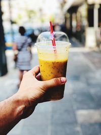 Close-up of hand holding drink in disposable glass on footpath