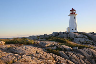 Lighthouse amidst rocks and buildings against sky