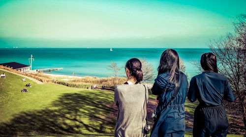 Rear view of people standing at beach against sky