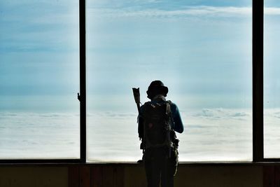 Man standing by window against sky