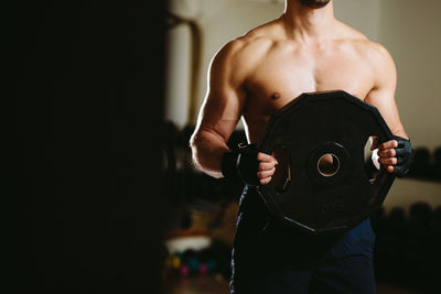 Midsection of shirtless man holding weights at gym