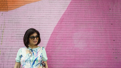 Portrait of woman standing against pink wall