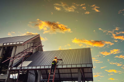 Low angle view of man working on building against sky