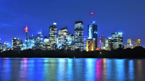 Illuminated buildings by river against sky at night