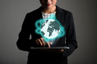 Digital composite image of smiling woman using tablet below globe icon against gray background