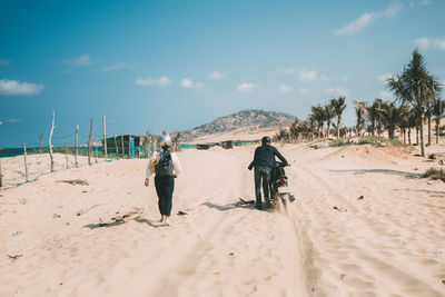 Rear view of men riding horse on beach against sky