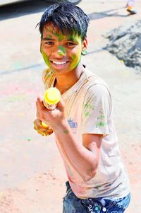 Portrait of smiling teenage boy holding water gun during holi at beach