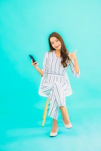 Young woman using phone while standing against blue background