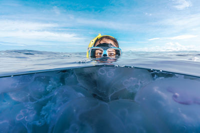 A woman in a black wetsuit is in the water with jellyfish. the jellyfish are floating around her