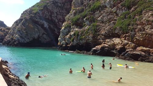 People swimming in sea against rock formations