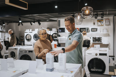 Salesman advising senior woman in buying appliance at electronics store