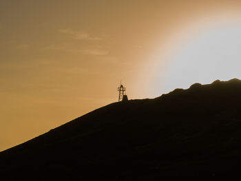 Silhouette of lighthouse by building against sky during sunset
