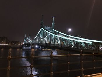 Illuminated bridge over river against sky at night