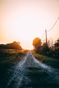 Surface level of road amidst plants on field against sky during sunset