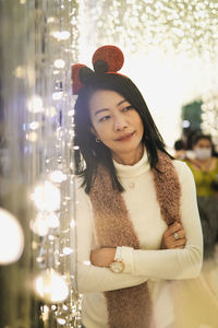 Portrait of young woman standing against illuminated christmas