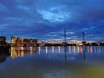 Illuminated buildings by river against sky at dusk