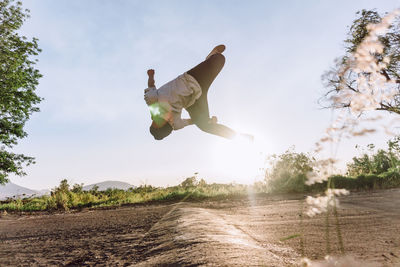 Acrobatic male jumping above ground and performing dangerous parkour trick on sunny day