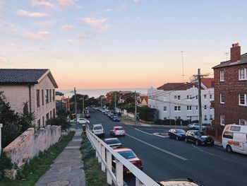 Cars on road amidst buildings against sky during sunset