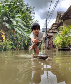 Cute boy reaching floating wood in water on street