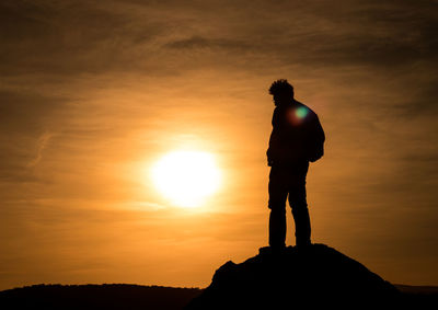 Silhouette man standing on rock against sky during sunset