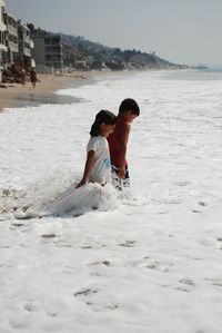 Happy siblings playing in sea against sky